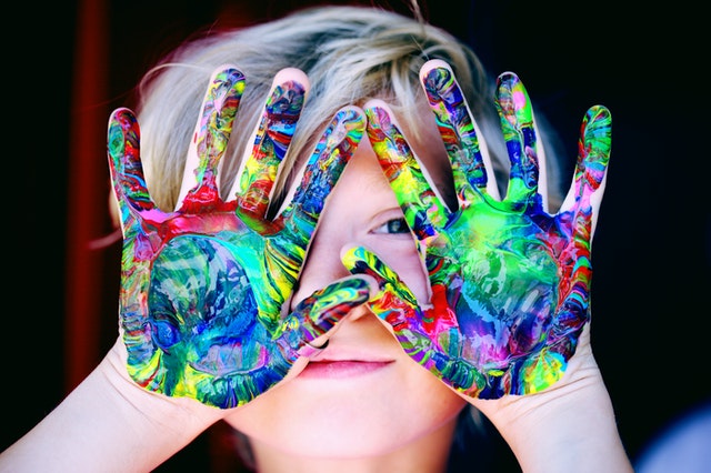 Child holding up painted hands. Find childcare for your child with autism.