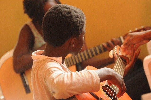 Boy playing guitar with teacher. How music therapy benefits a child with autism.