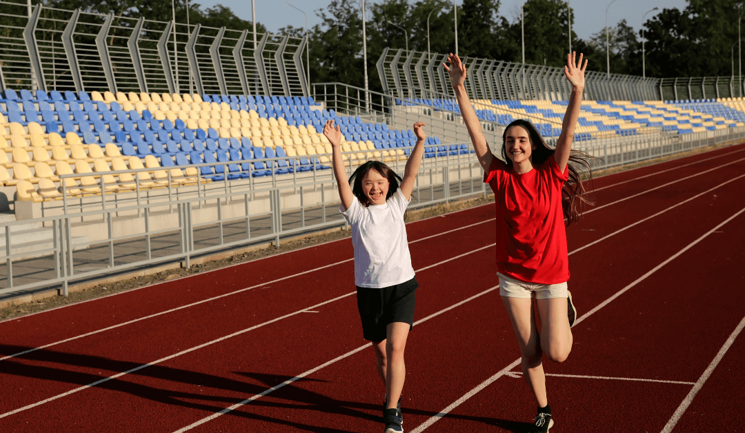 Two girls running with hands up on a track.