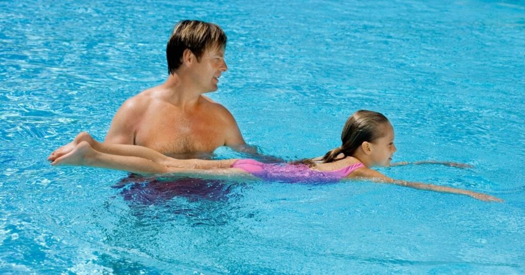 Man helping girl swim. Teaching your autistic child how to swim can be life saving.