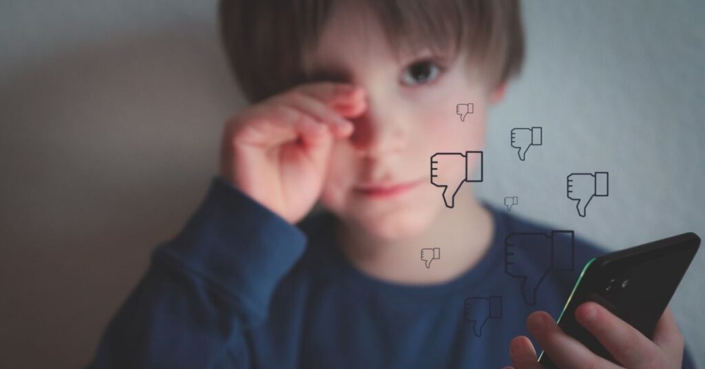 Boy holding phone and crying with Facebook thumbs down symbols. Learn how cyberbullying prevention can help your child with autism.