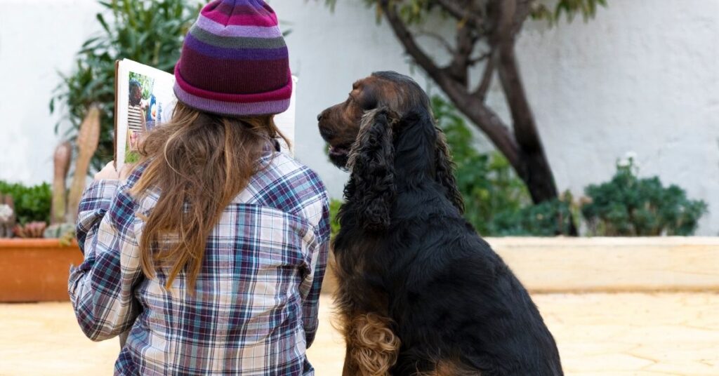 Girl sitting and reading a book to her dog. What is the best dog for your child with autism?