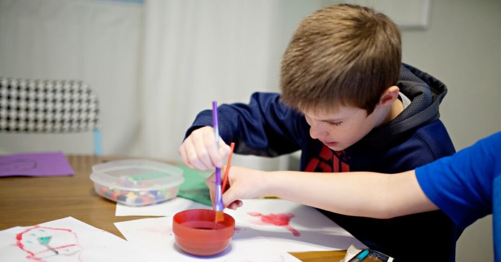 Boy using water color paints at a table. How art therapy can help children with autism and ADHD.