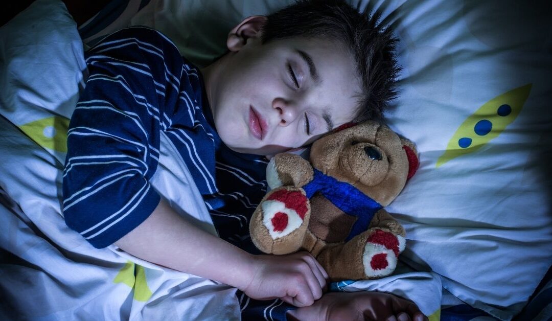 Boy sleeping with teddy bear in bed.