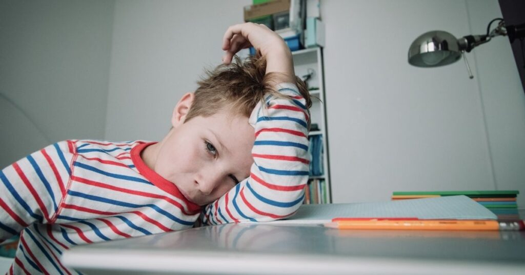Boy lying his head down on a desk with while chewing on his shirt. Should you encourage or discourage your autistic child's stimming?
