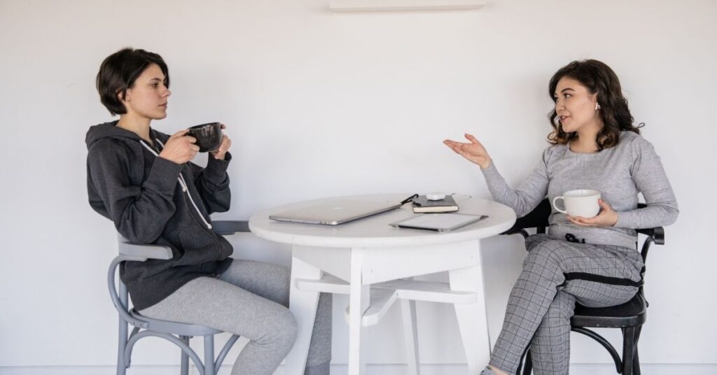 Two women sitting at a table talking and drinking coffee. What to do if you think your friend's child may have autism.