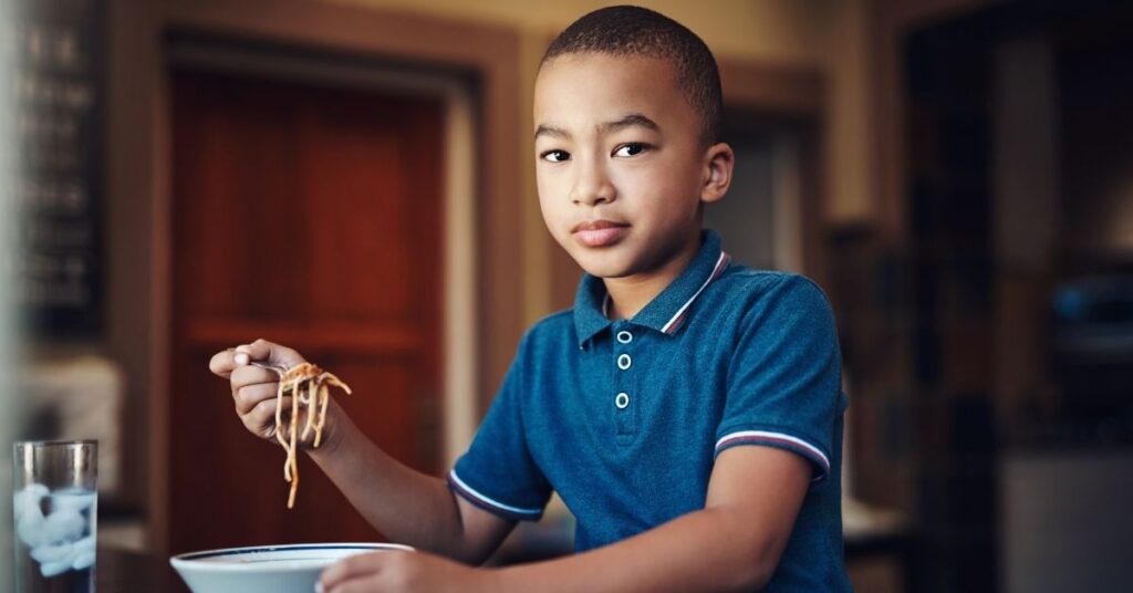 Boy sitting at table and eating a bowl of pasta. How to help deal with picky eating with your child with autism and ADHD.