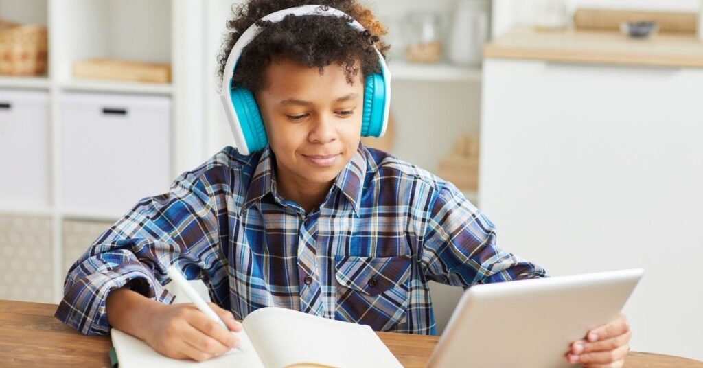 Boy sitting at a desk wearing headphones with a notebook and computer. How can you help your autistic and ADHD student to develop effective study habits?