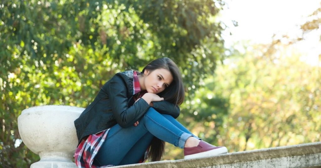 Depressed teen girl sitting on a ledge. Could you child with autism and ADHD also have depression?