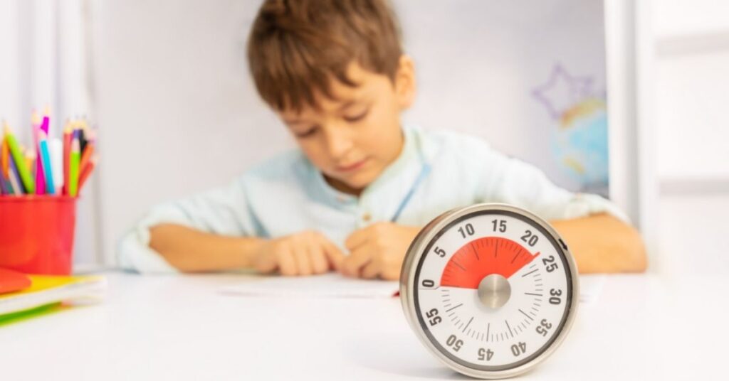 Boy sitting at a table or desk writing with a timer in front of him. How can you help your autistic and ADHD student develop effective study habits?