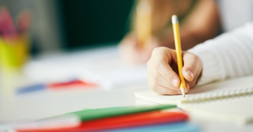 Child writing with pencil. How can technology help your autistic child improve their reading and writing skills?