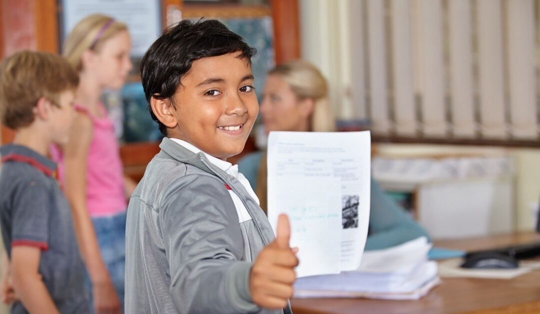 Boy holding a paper with a good grade on it and giving the thumbs up