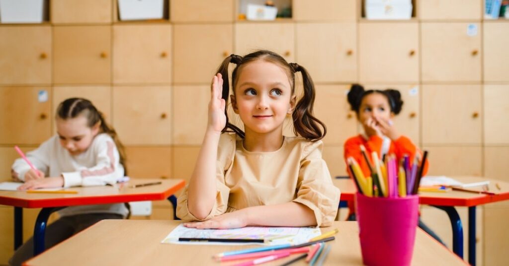 Girl sitting at desk and raising her arm in class. How can a behavior intervention plan help your child with autism and ADHD?