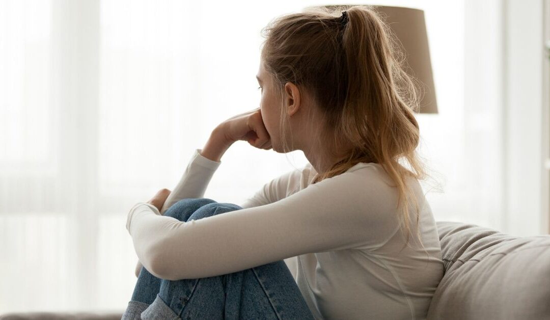 Woman with head in hand and looking out the window. Feeling of loneliness.