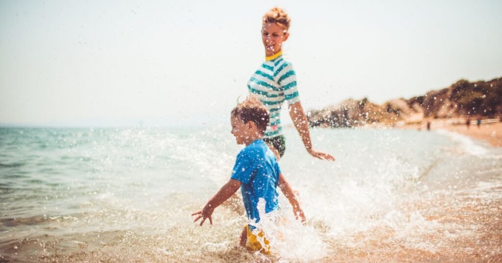 Mom with son playing in the water on a beach. How can you help your autistic child progress over the summer?