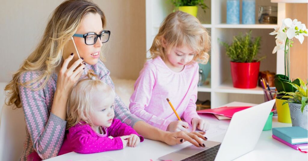 Mom sitting with daughters, talking on the phone and looking at the computer. How to organize all the paperwork for your autistic child.