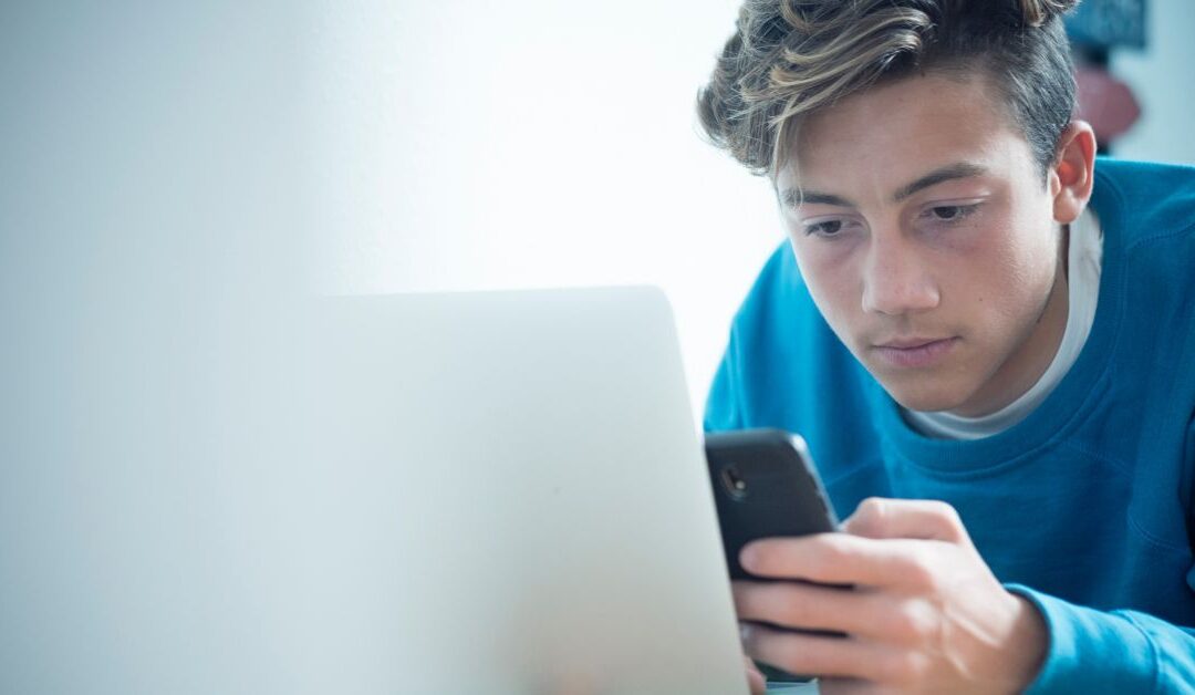 Teen boy holding his phone and looking at computer