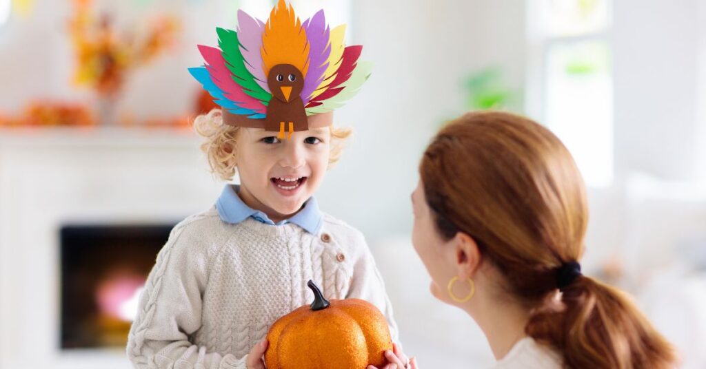 Boy with a turkey headband on and holding a pumpkin, smiling and talking to his mom. Reasons to be thankful for autism.