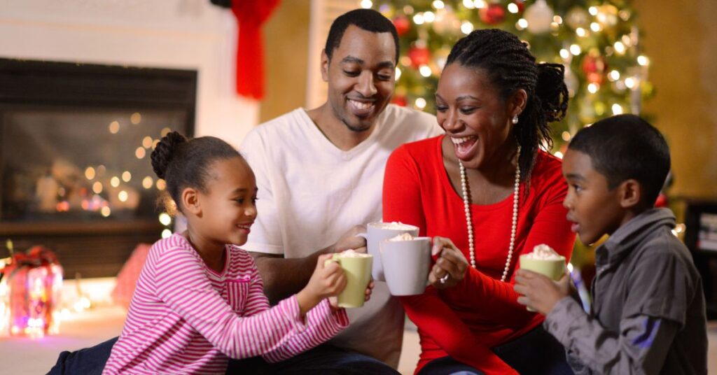 Family in front of Christmas tree toasting with hot cocoa. How can you prepare relatives for holidays with your autistic child?