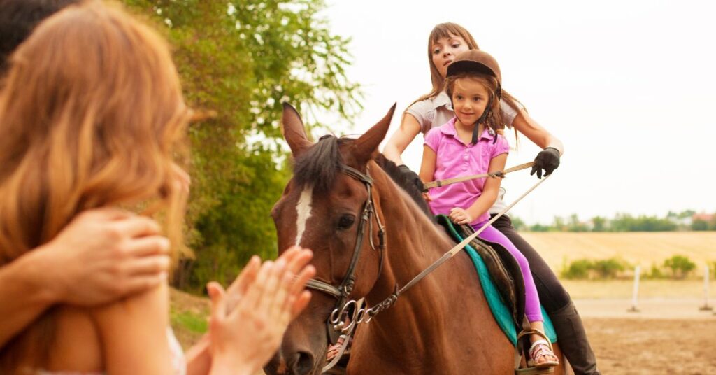 Girl riding horse with therapist and parents looking on