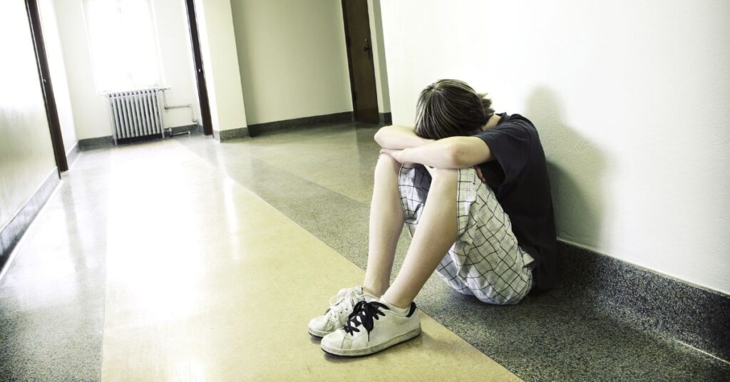 Teen boy sitting along school wall with head down. Does your teen with ADHD struggle with rejection sensitive dysphoria?