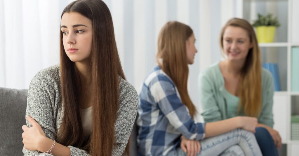 Teen girl sitting by herself while others are behind her, feeling rejected. Does your teen with ADHD struggle with rejection sensitive dysphoria?