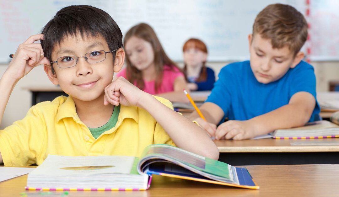 Boy sitting at desk with book open in classroom
