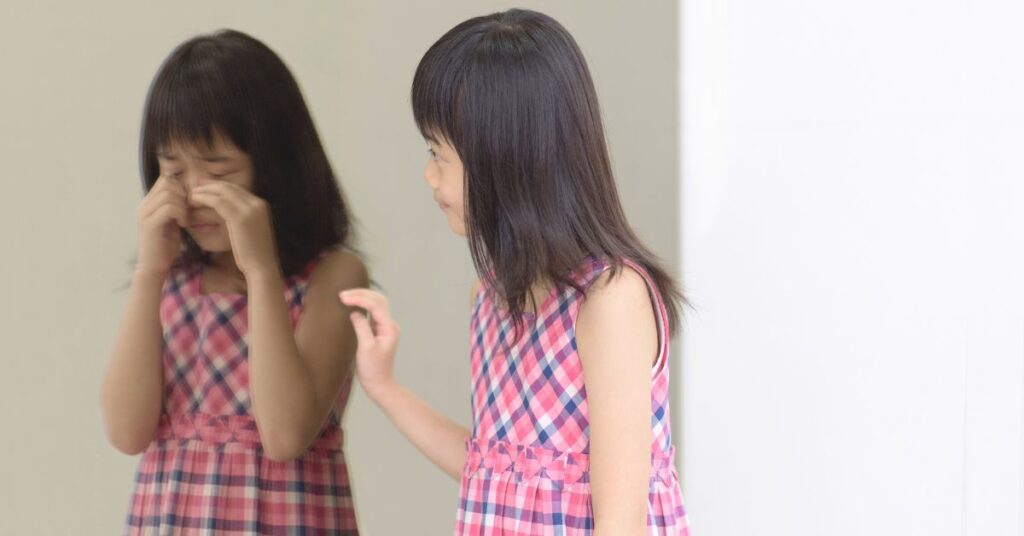 Girl looking at her image in the mirror, trying to comfort her image that is crying. How can you help your child with autism and ADHD improve their self-esteem?