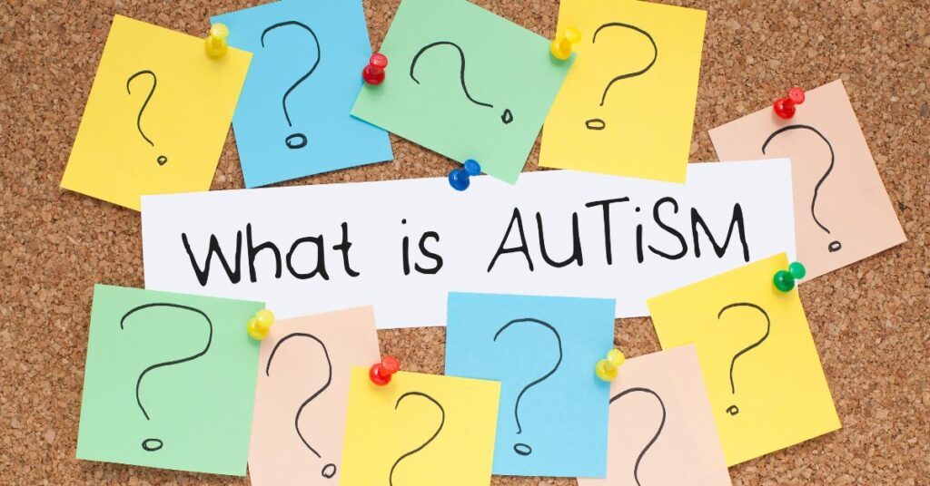 Corkboard that has "What Is Autism?" posted on it with post-it notes with question marks. How do you tell your child they have autism?