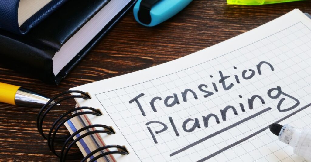 Notebook with "Transition Planning" written on it, sitting next to a pencil and books on a desk. How can we help our autistic children transition into autistic adults well?