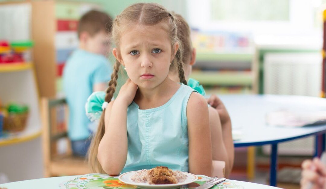 Girl sitting at a table in front of a plate of food looking concerned