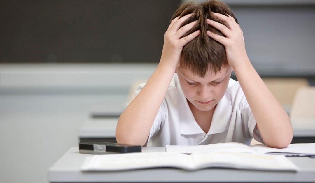 Boy sitting in front of his book holding his head, looking confused and frustrated.