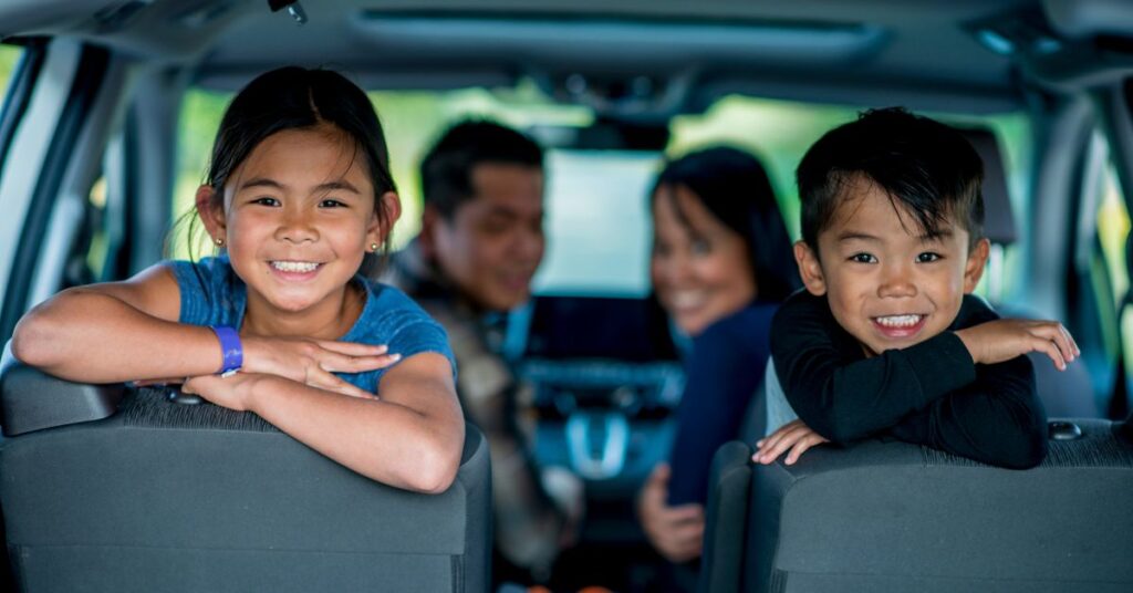 Family sitting in car smiling. How can you make road trips more fun for your autistic child?