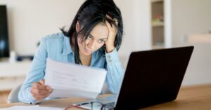 Woman looking at a bill and computer with a concerned look on her face. How can you pay for the care and services your child with autism needs?