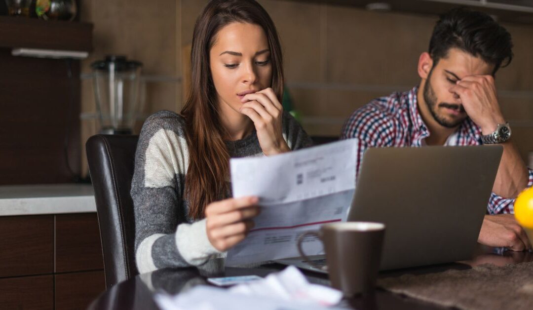 Man and woman sitting at computer and looking at bills with worried looks