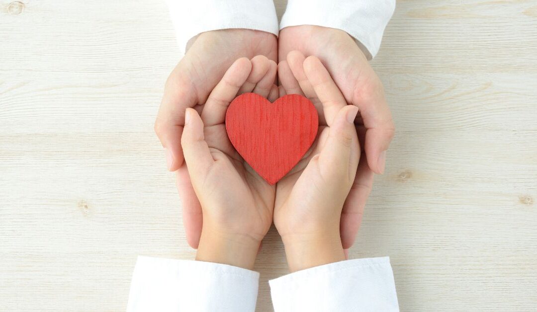 Parent and child hands overlapping to hold a red heart