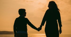 Silhouette of mother and boy holding hands, walking and looking at each other. Be inspired by autism, ADHD and parenting quotes.