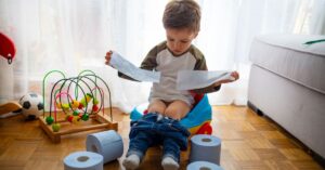 Little boy sitting on a training potty with toilet paper rolls sitting around him