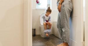 Girl sitting on toilet with her mom standing beside her. Overcoming toilet training challenges for children with autism.