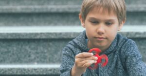 Boy looking at a fidget spinner. How sensory toys can help your child with autism and ADHD.