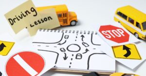 Toy bus and van with post-it notes saying "driving lesson" with intersection drawing and stickers of street signs. How can you help your teenager with autism stay safe while driving?
