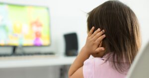 Girl putting her hand over her ear while watching a video on the computer