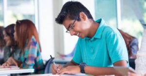 Teen boy writing notes in class. How can you help your teen with autism and ADHD take more effective notes?