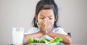 Girl with her hands over her face looking at a plate of salad and refusing to eat. When should you seek nutrition counseling for your child with autism?