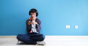 Teenage boy sitting on the floor against the wall wearing headphones and looking at his phone. What are the autism levels and how can they explain where your child falls on the autism spectrum disorder?