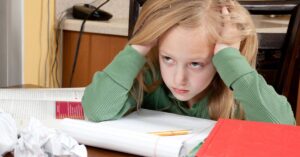 Girl sitting with homework with her hands in her hair looking frustrated. How does a lack of executive function skills hold back your child with autism and ADHD?