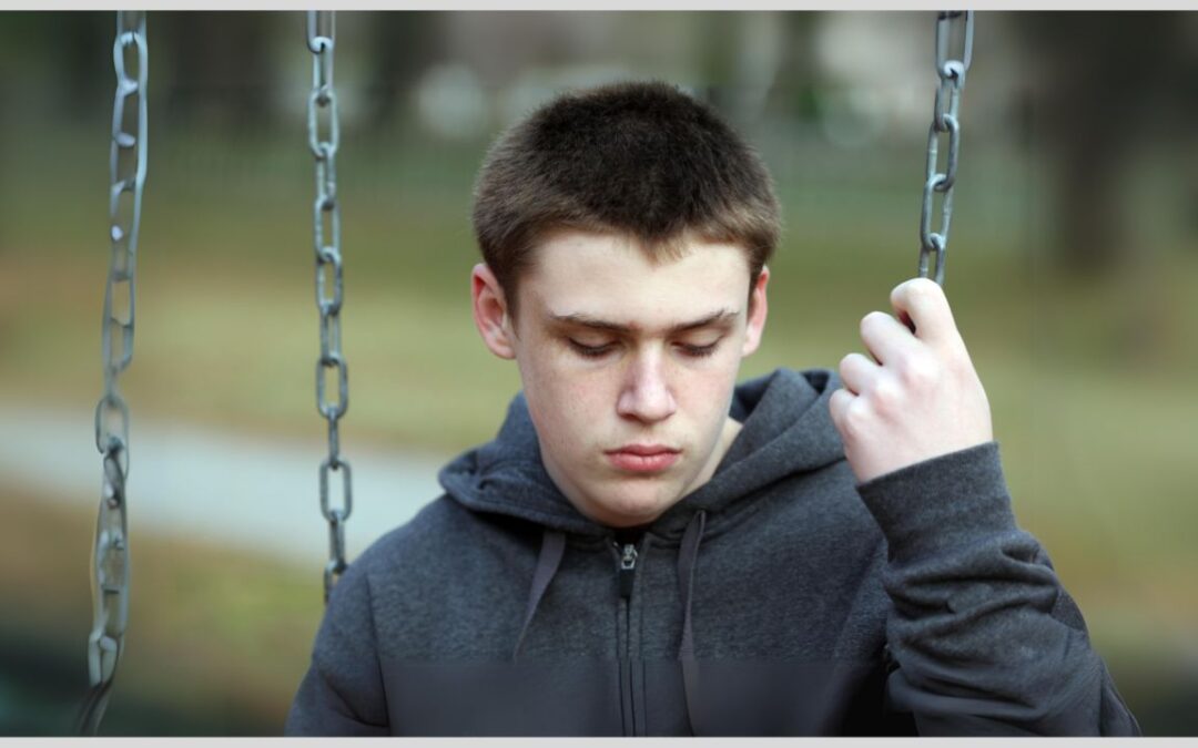 Teenage boy sitting on a swing, looking sad