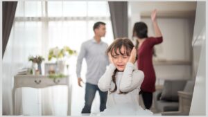 Parents arguing in background with little girl crying with hands over her ears in the forefront. Effects of divorce on children with autism