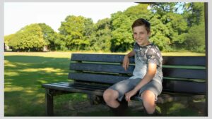 Teenage boy sitting on bench in park. How to help your autistic teenager during their adolescent years.