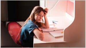 Teen girl sitting at a desk with notebook in front of her. How can you help your autistic child or teen improve their resilience?